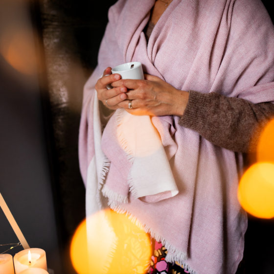 Une femme enveloppée dans un châle rose tient une tasse.