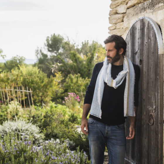 Un homme portant une écharpe bleue et beige se tient près d'une porte en bois.